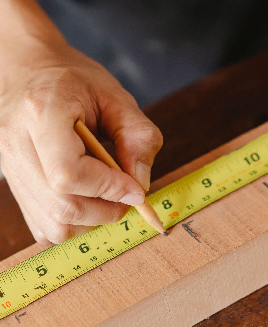 Carpenter marking a board with a pencil and tape measure